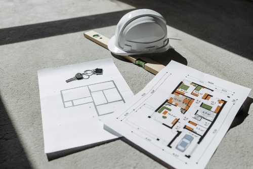 Construction helmet, house floor plans, level tool, and keys on a concrete floor